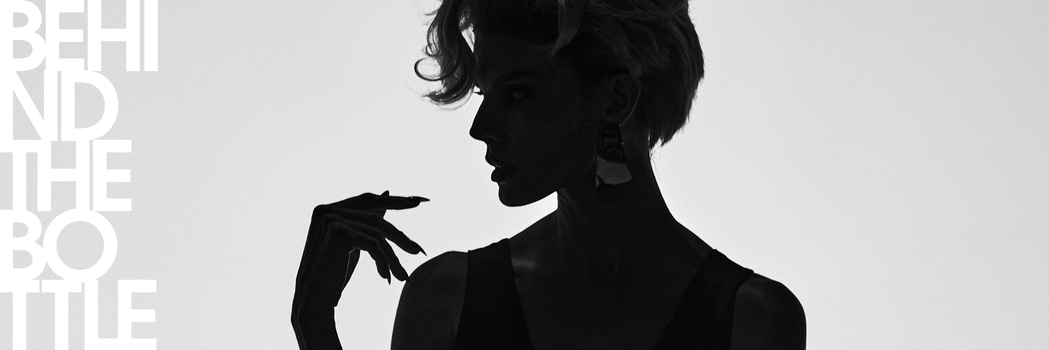 Black and white editorial-style image with large white text reading 'BEHIND THE BOTTLE' and a silhouetted woman in profile